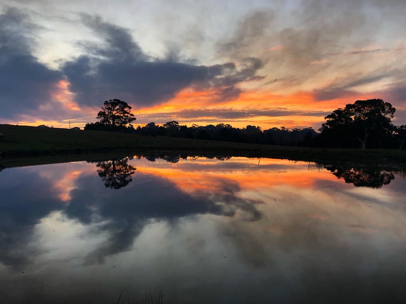 A fiery orange sunset mirrored perfectly in the still water of the farm dam
